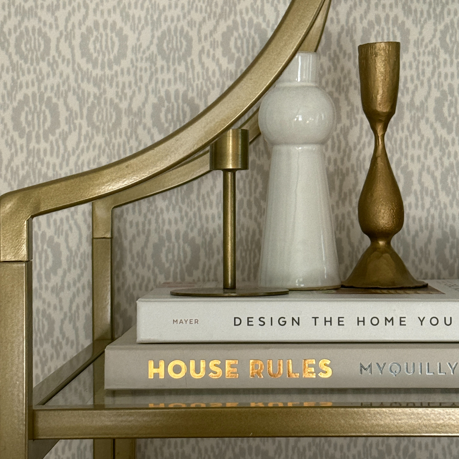 Decorative setup with books  and a candle holder on a surface with a patterned wall background.