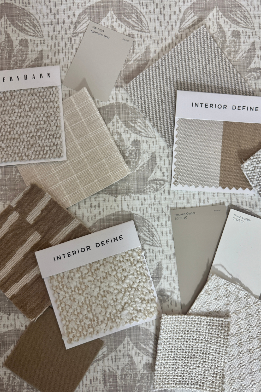 Collection of fabric swatches and samples with 'Interior Define' labels on taupe wallpaper